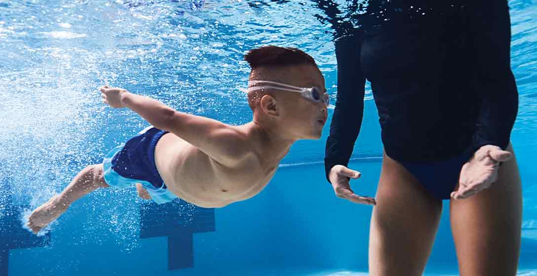 A young boy swimming alongside an instructor at the Life Time pool