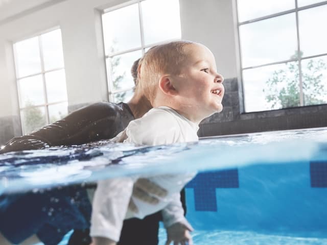 A young boy swimming with an instructor in an indoor pool
