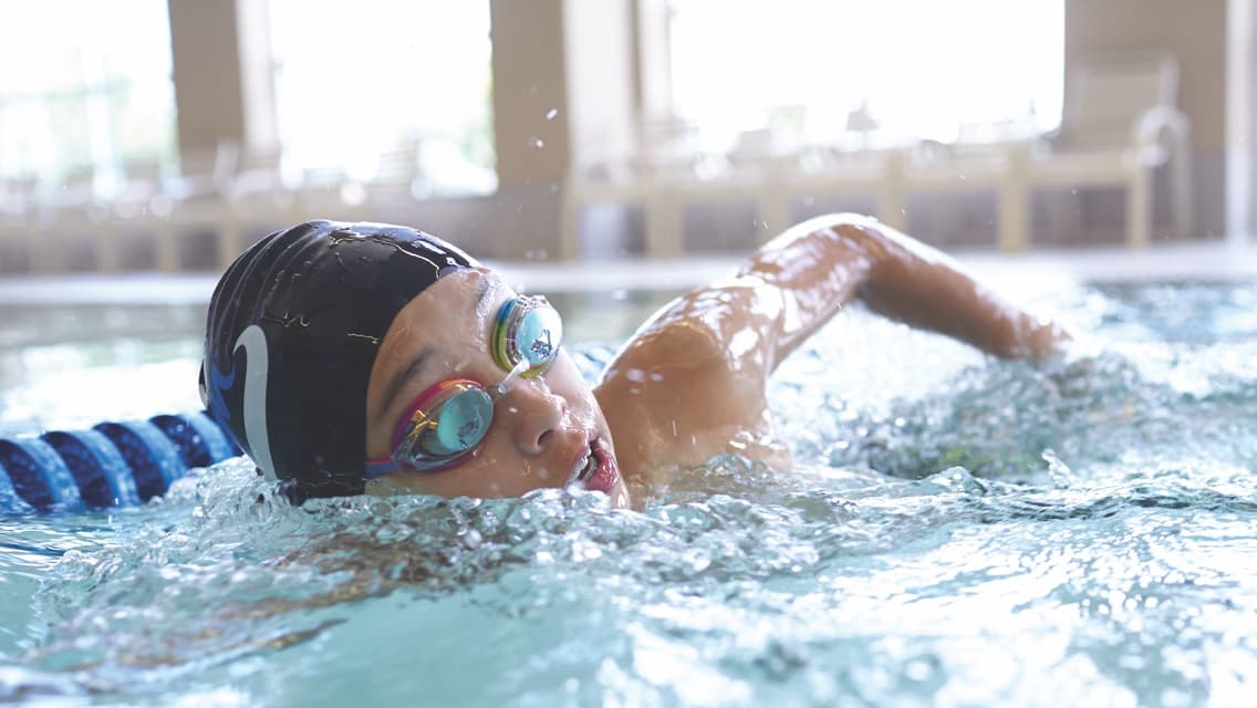 Young boy doing the freestyle stroke while taking a breathe in a lap pool